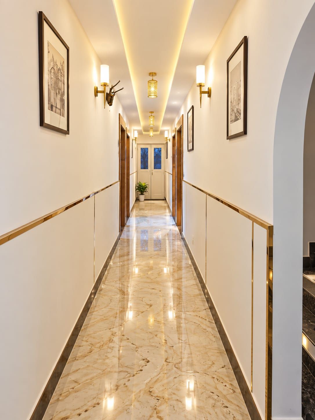 A hallway with marble flooring, wall-mounted light fixtures, and framed artwork.