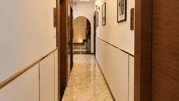 A hotel hallway with marble flooring, wooden doors, and wall-mounted lighting.