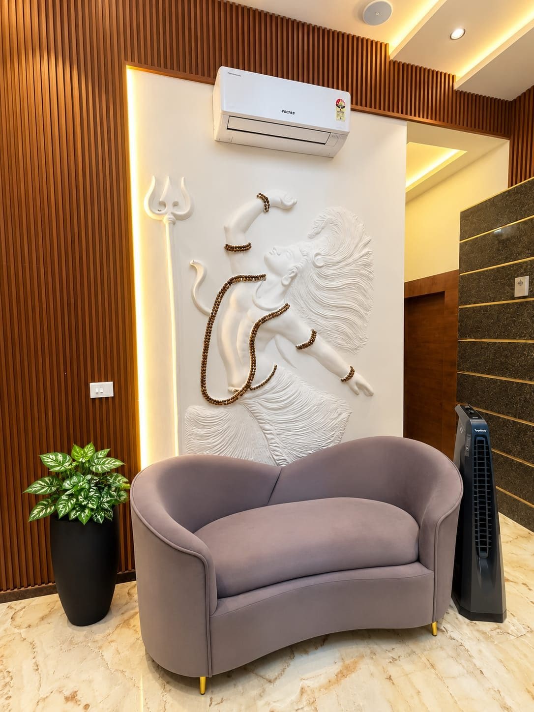 A modern interior with a grey sofa, a decorative wall with a relief sculpture, an air conditioning unit, and a black speaker.