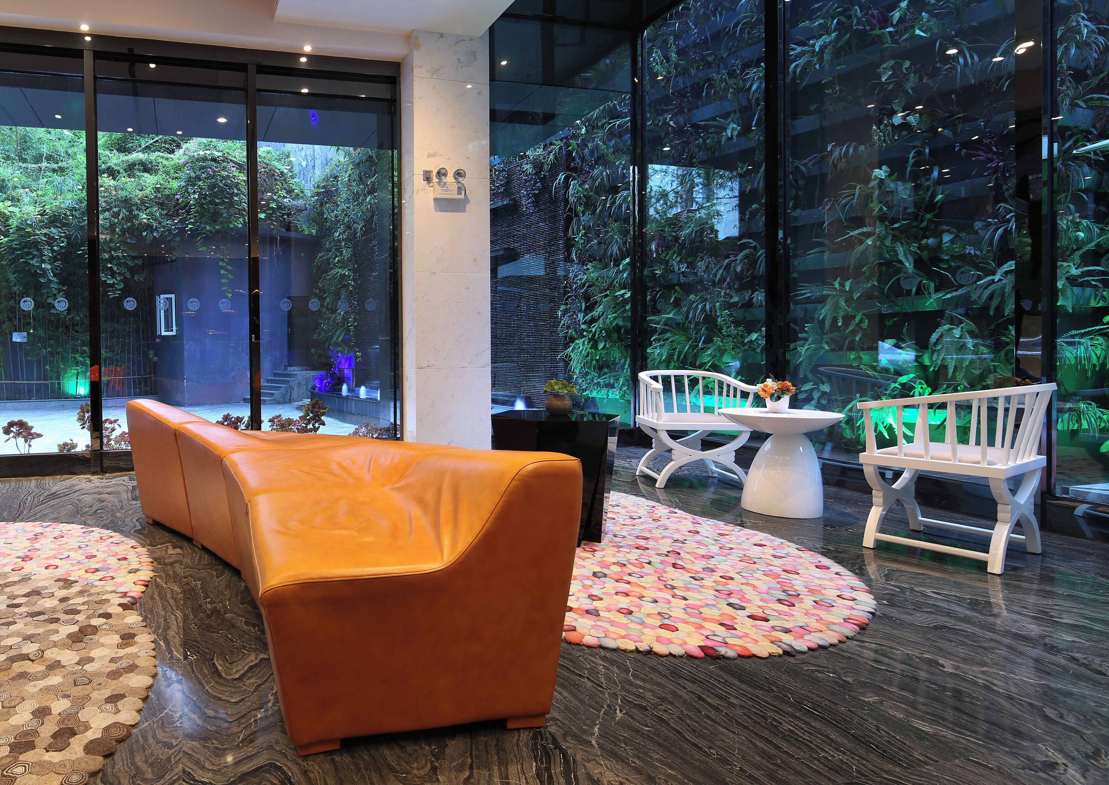 A modern interior with a seating area, a glass wall with a view of greenery, and a decorative rug.