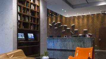 Un hall con mostrador de recepción, una estantería, un sofá de cuero, un sillón naranja y un suelo estampado.