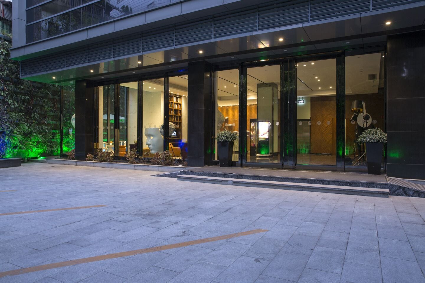 A modern hotel entrance with glass doors, a tiled pavement, and indoor lighting.