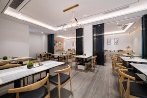 A modern dining area with multiple tables and chairs, a central light fixture, and a kitchen in the background. - Paco Hotel Taojin Metro Guangzhou (Guangzhou)