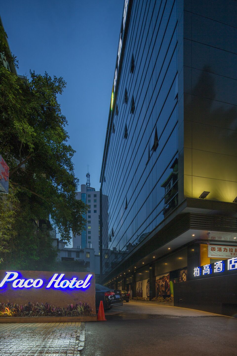 Entrada de hotel con un letrero de neón, pavimento mojado y un edificio con ventanas reflectantes.