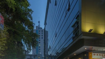 Entrada de hotel con un letrero de neón, pavimento mojado y un edificio con ventanas reflectantes.