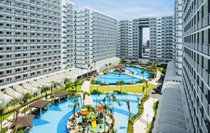 A high-rise hotel with multiple balconies, a central swimming pool, and a children's play area. - Serene 1-bedroom Apartment With Shared Pool in Pasay (Pasay)