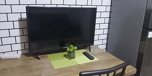 A television on a stand with a remote control and a small plant on a green mat. - Serene 1-bedroom Apartment With Shared Pool in Pasay (Pasay)