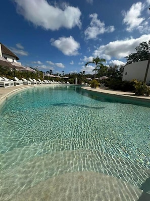 A clear swimming pool with lounge chairs and umbrellas, surrounded by buildings and greenery. - Hotel Mundo Maya Nuevo Uxmal (Ciudad del Carmen)