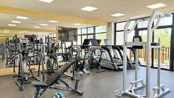 Un gimnasio con diverso equipo de ejercicio, ventanas amplias y vistas al exterior.