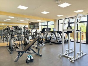 A gym with various exercise equipment, large windows, and a view of the outdoors.
