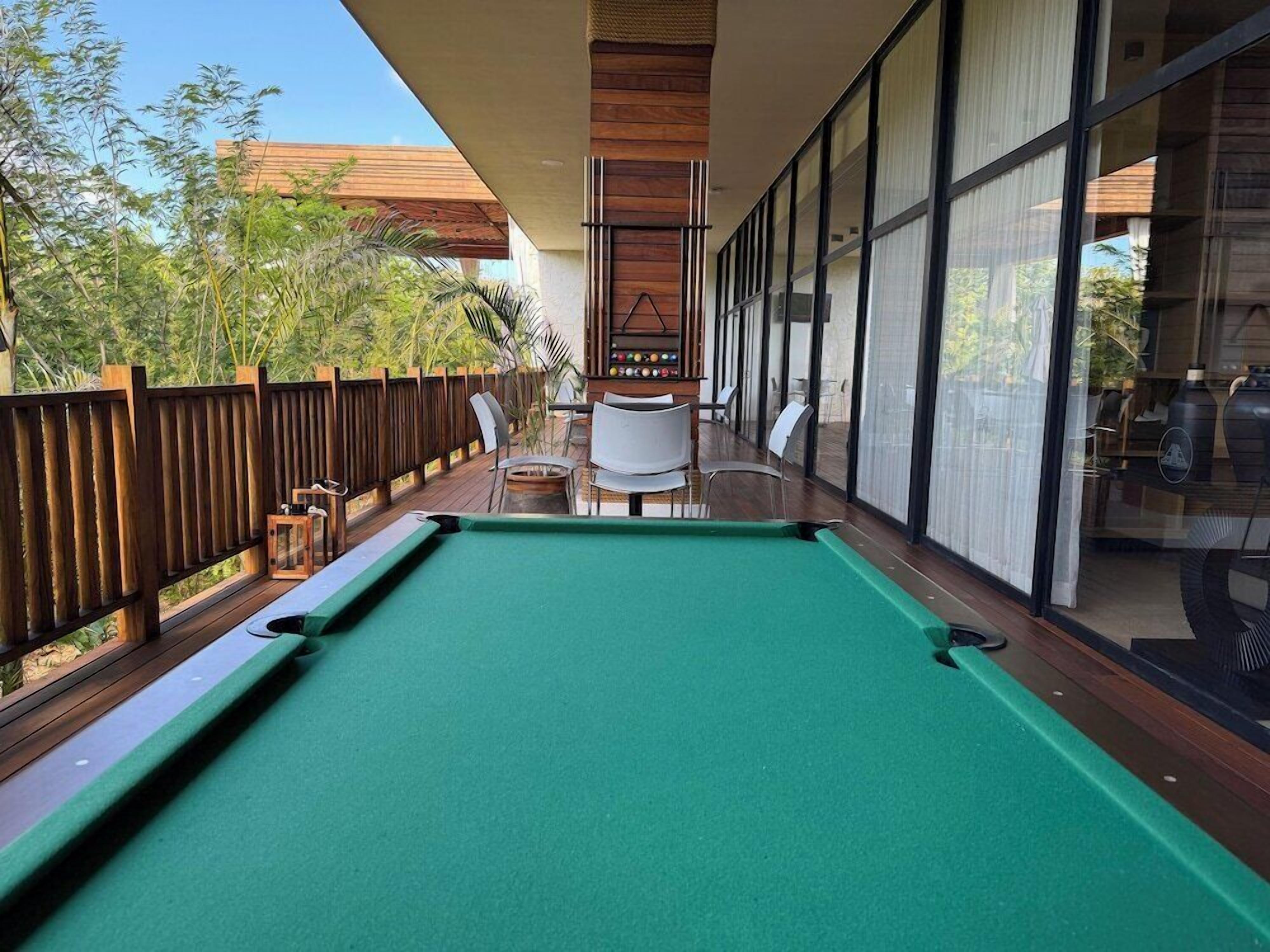 Mesa de billar en una terraza con sillas y valla de madera.