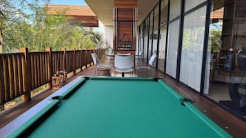 Mesa de billar en una terraza con sillas y valla de madera.