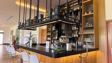 Una zona de bar con mostrador, taburetes y estantes llenos de botellas y vasos.