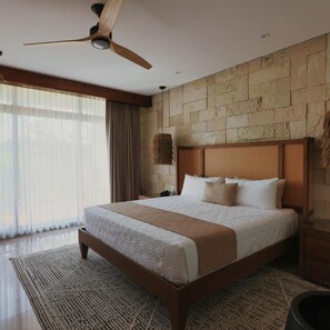 A spacious bedroom with a large bed, a ceiling fan, stone wall, and a view of the outdoors.