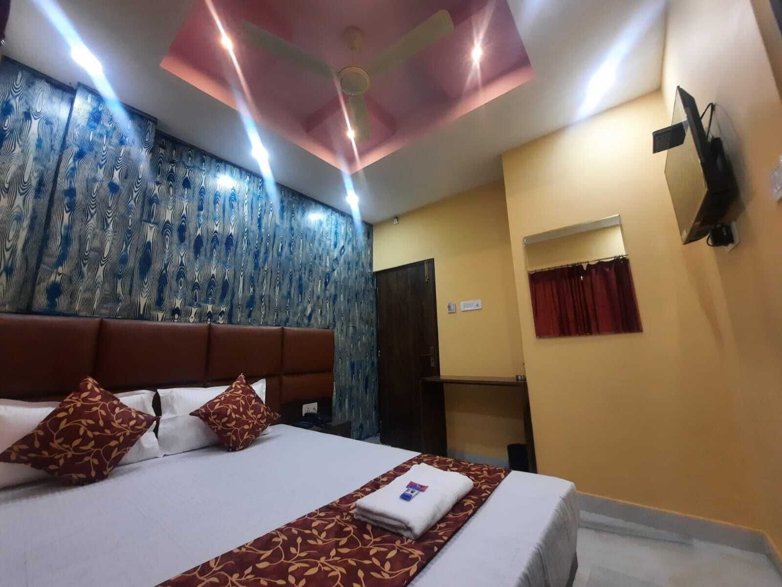 A hotel room with a bed, a ceiling fan, a wall with a patterned design, and a window with curtains.