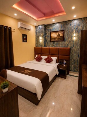 A hotel room with a bed, a nightstand, a desk, and a wall-mounted air conditioner.