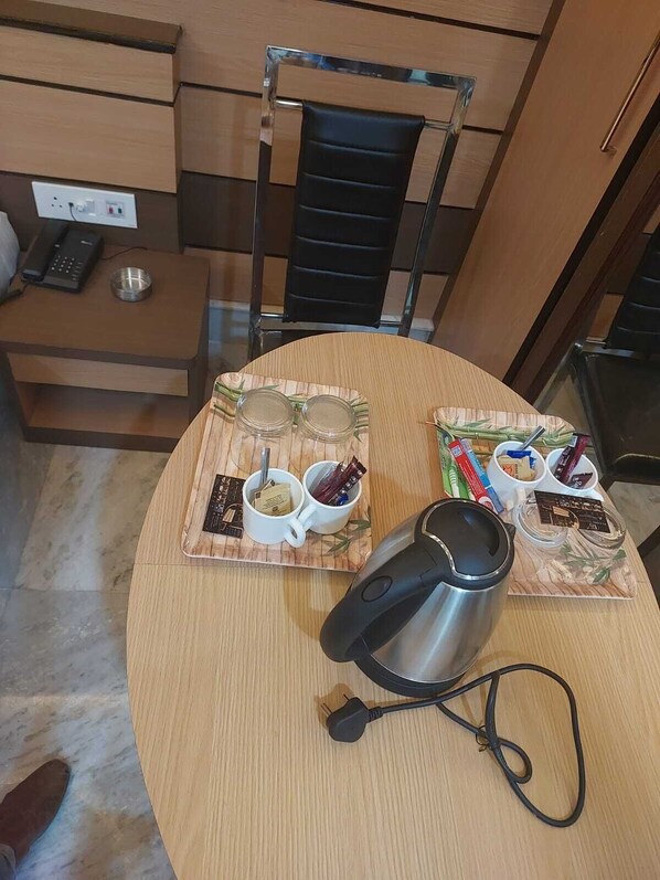 A round dining table with a coffee maker, two mugs, and condiments on placemats.