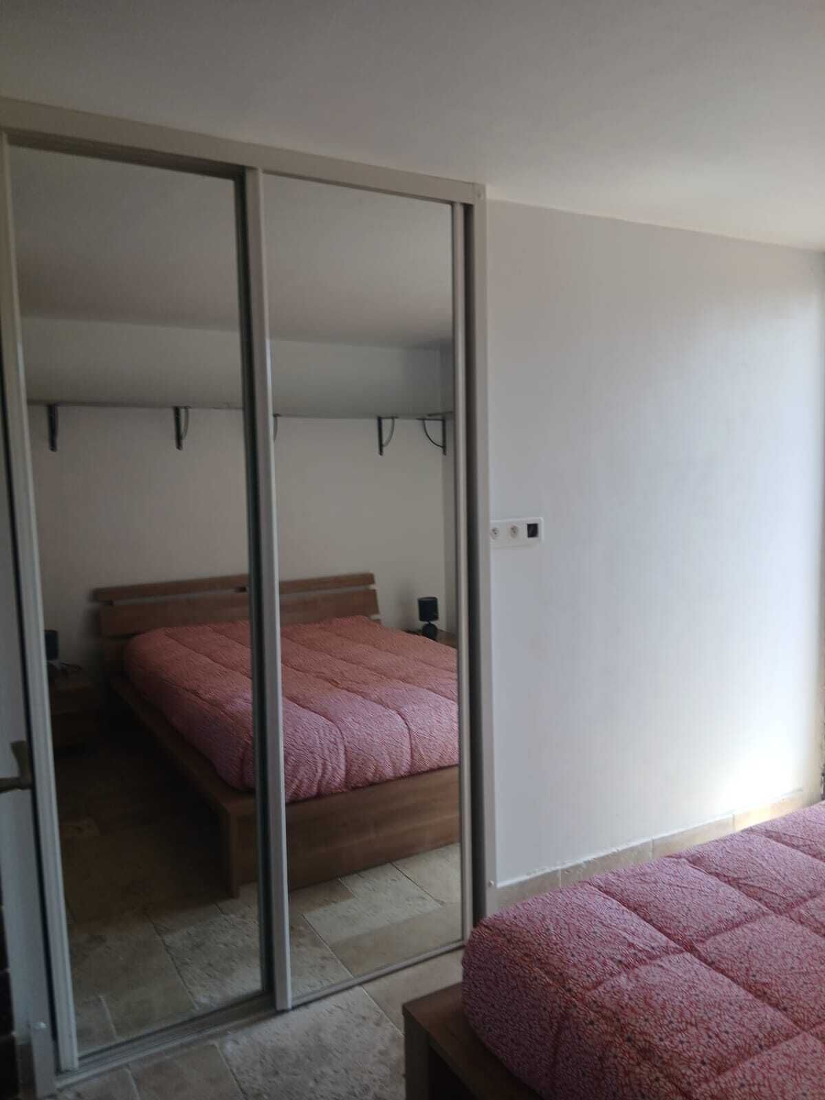 Un dormitorio con una puerta corredera que da a un baño, una cama con una manta rosa y una mesita de noche con una lámpara.