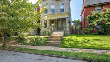 A two-story stone house with a front porch, a set of stairs leading to the entrance, and a well-maintained lawn.