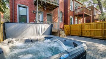 Un jacuzzi dans un jardin, avec une maison en briques et une clôture en bois.