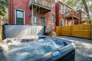 A hot tub in a backyard with a brick house and a wooden fence.