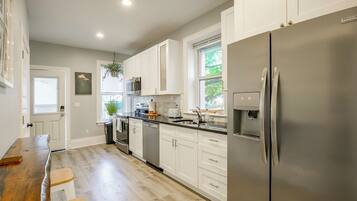 A modern kitchen with white cabinetry, stainless steel appliances, and a wooden dining table.