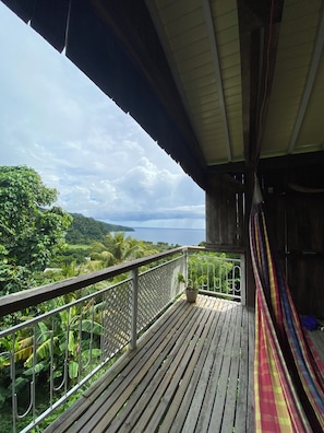 Terraza de madera con barandilla, una hamaca y vistas a un paisaje exuberante y un cuerpo de agua.