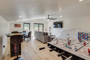 A modern living space with a foosball table, a dining area, and a large window offering a view of the outdoors. - Game Room & Stunning Mtn Views! Cedar City Home (Cedar City)