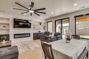 Ein modernes Wohnzimmer mit Deckenventilator, Flachbildfernseher, Kamin und Essbereich mit Tisch und Stühlen.