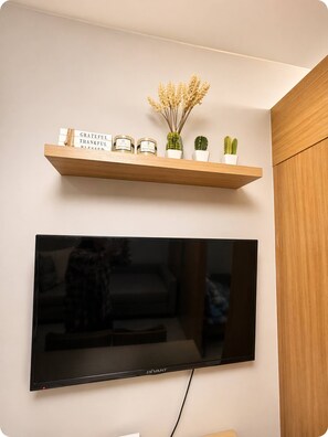 A flat-screen TV mounted on a wall with a wooden shelf above it holding candles and small potted plants. - Vibrant Studio Apartment in Vibrant Pasay, Philippines (Pasay)