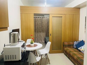 A compact living space with a kitchenette, a dining area with a table and chairs, a sofa, and a sliding door closet. - Charming 1-Bedroom Apartment Near Mall of Asia (Pasay)