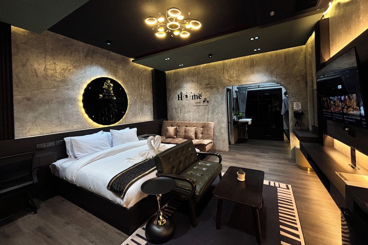 A modern hotel room with a large bed, a sofa, a small table, and a unique circular light fixture on the wall.