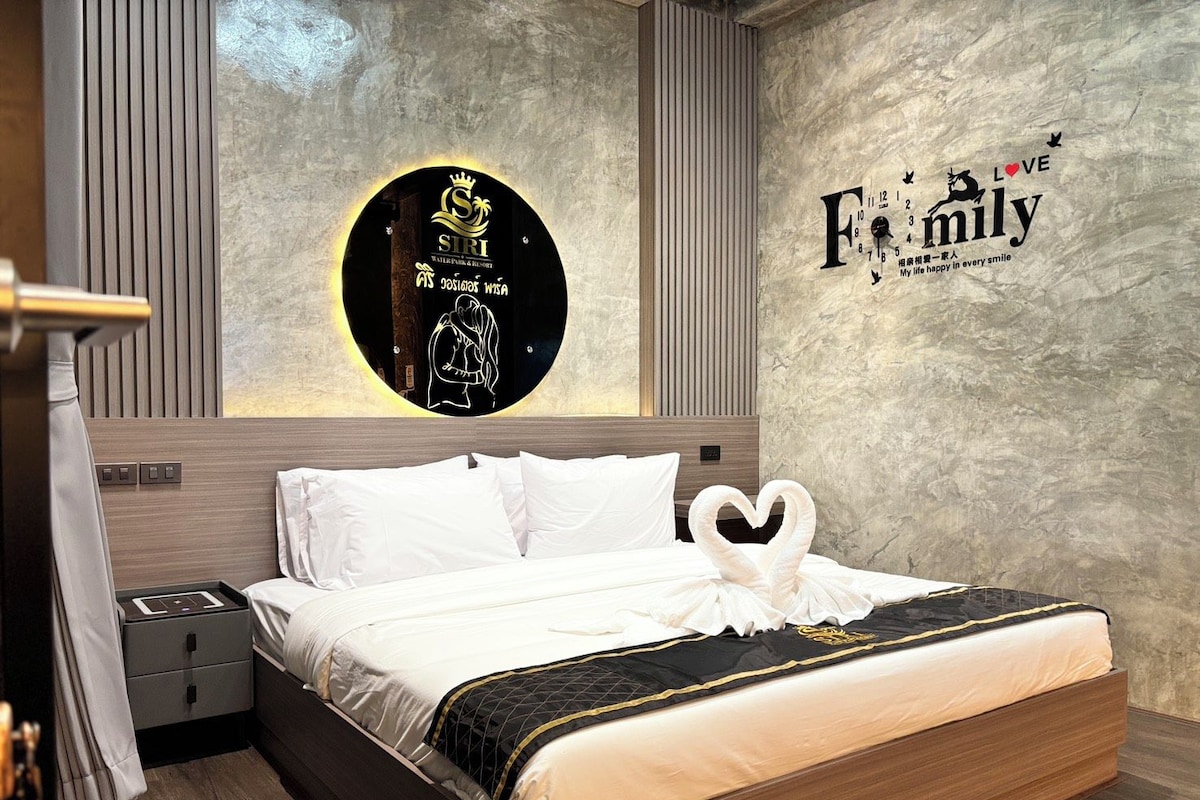 A modern hotel room with a bed, a nightstand, a wall clock, and a circular logo on the wall.