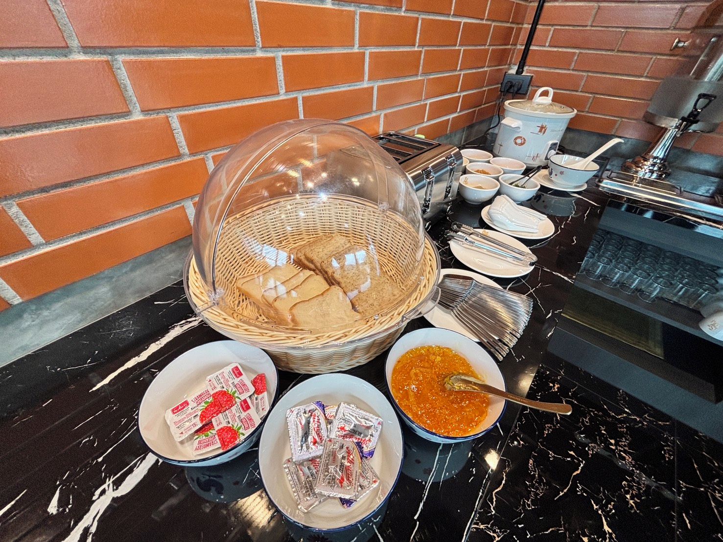 Mesa de mármol con un bufé de desayuno que incluye pan, mermeladas y untables.