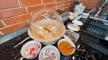 Mesa de mármol con un bufé de desayuno que incluye pan, mermeladas y untables.