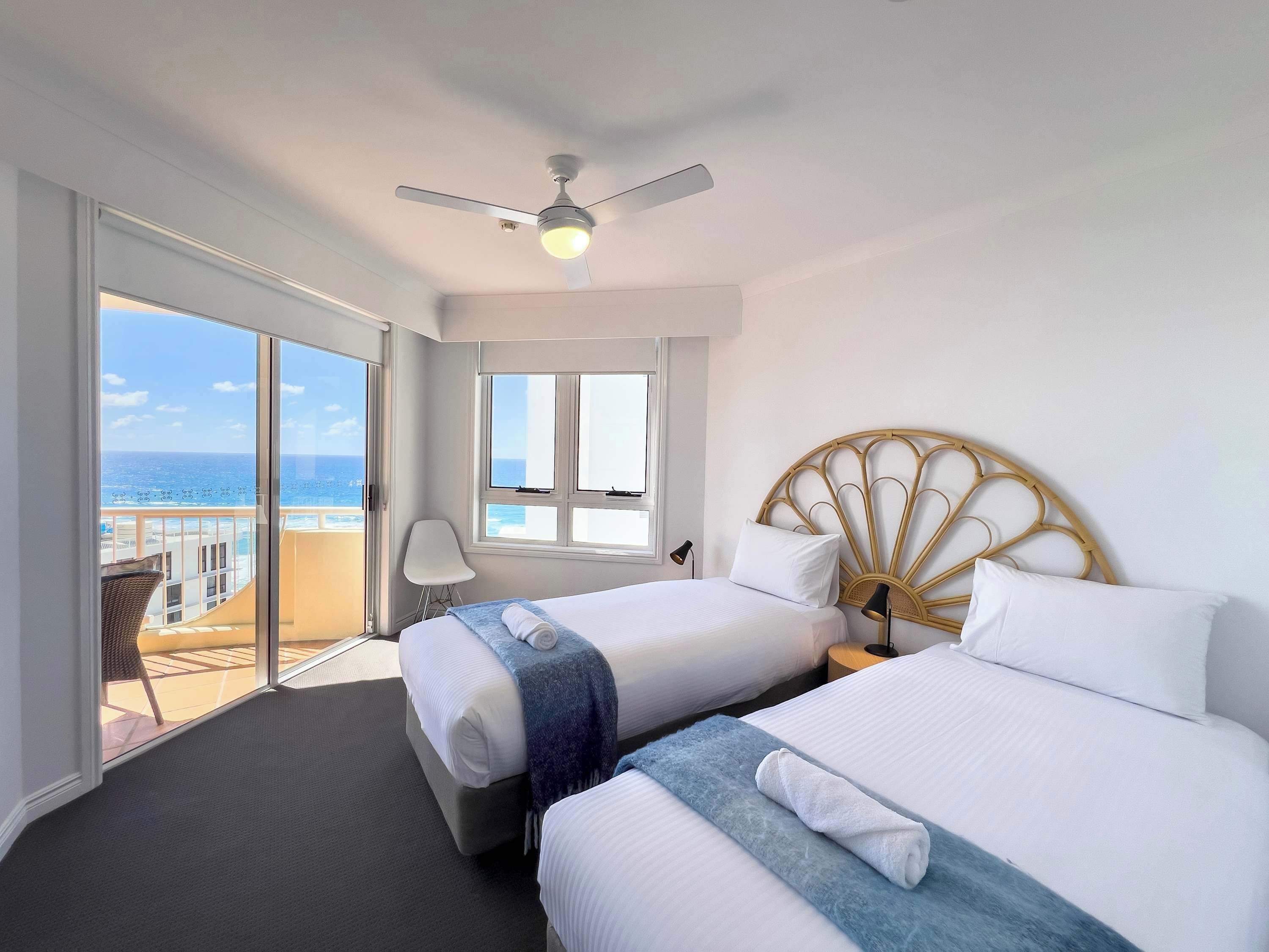 Ein Hotelzimmer mit zwei Betten, einem Deckenventilator, Meerblick und einem Balkon mit einem Stuhl.