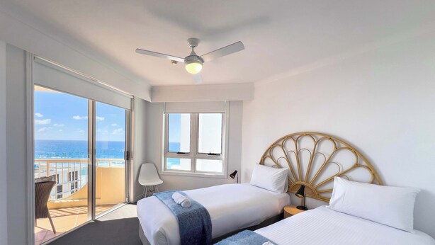 Et hotelværelse med to senge, en loftsvifte, havudsigt og en balkon med en stol.
