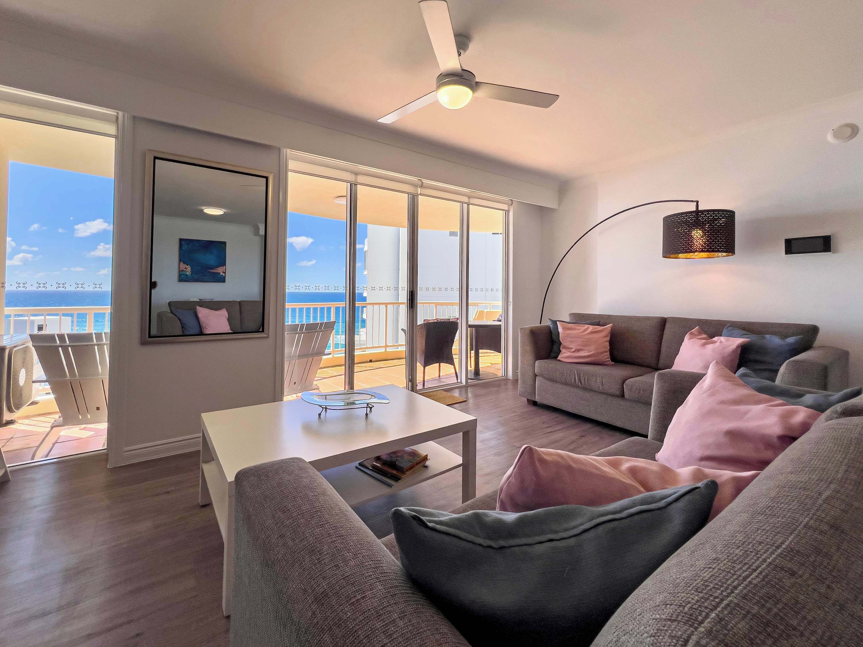 Una sala de estar moderna con balcón, ventilador de techo y vista al mar.