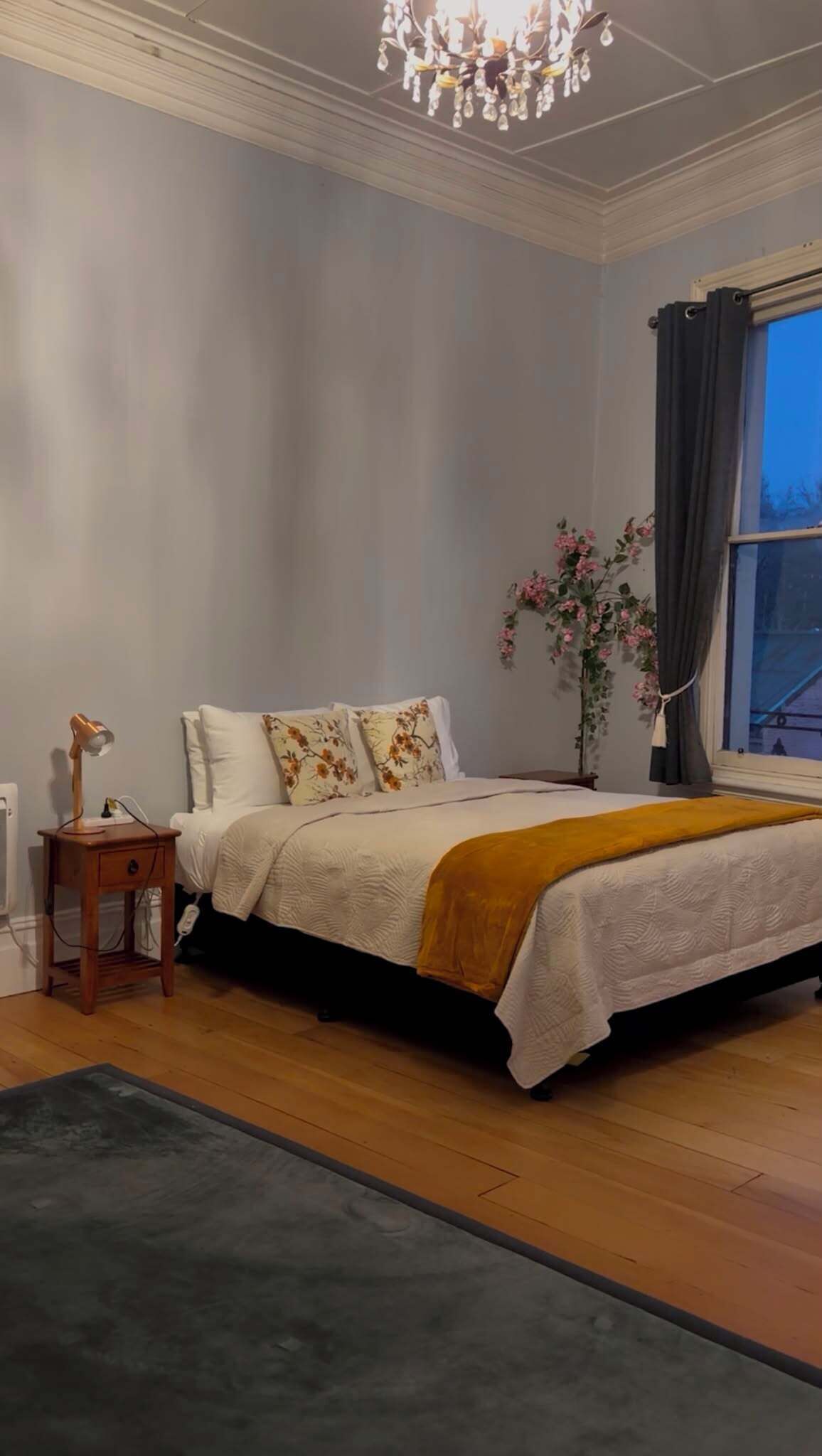A bedroom with a bed, bedside table, lamp, and a window with curtains.