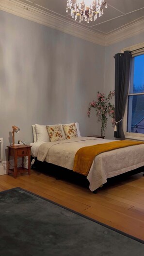Un dormitorio con cama, mesita de noche, lámpara y una ventana con cortinas.