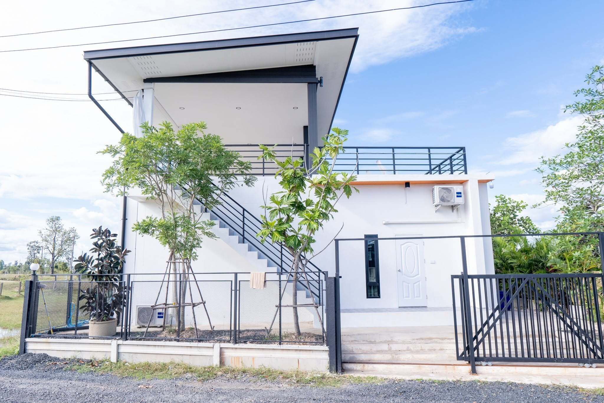 A modern two-story building with a covered entrance, a staircase, and a gated driveway.