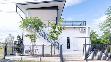 A modern two-story building with a covered entrance, a staircase, and a gated driveway.