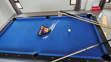 A pool table with a blue felt surface, a set of pool balls, and two pool cues.