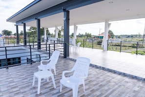 An outdoor covered area with white plastic chairs and a tiled floor.