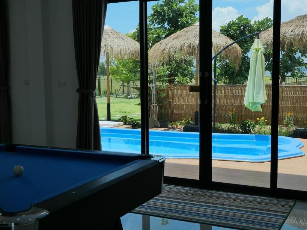 Una mesa de billar en una habitación con vista a una piscina en el patio y un parasol de paja.
