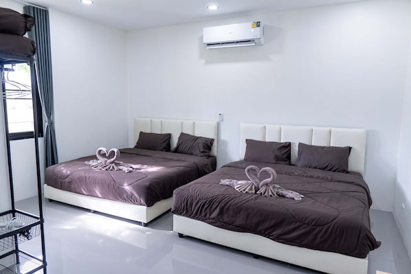 A hotel room with two beds, each with a heart-shaped towel decoration, a white headboard, and an air conditioning unit above.