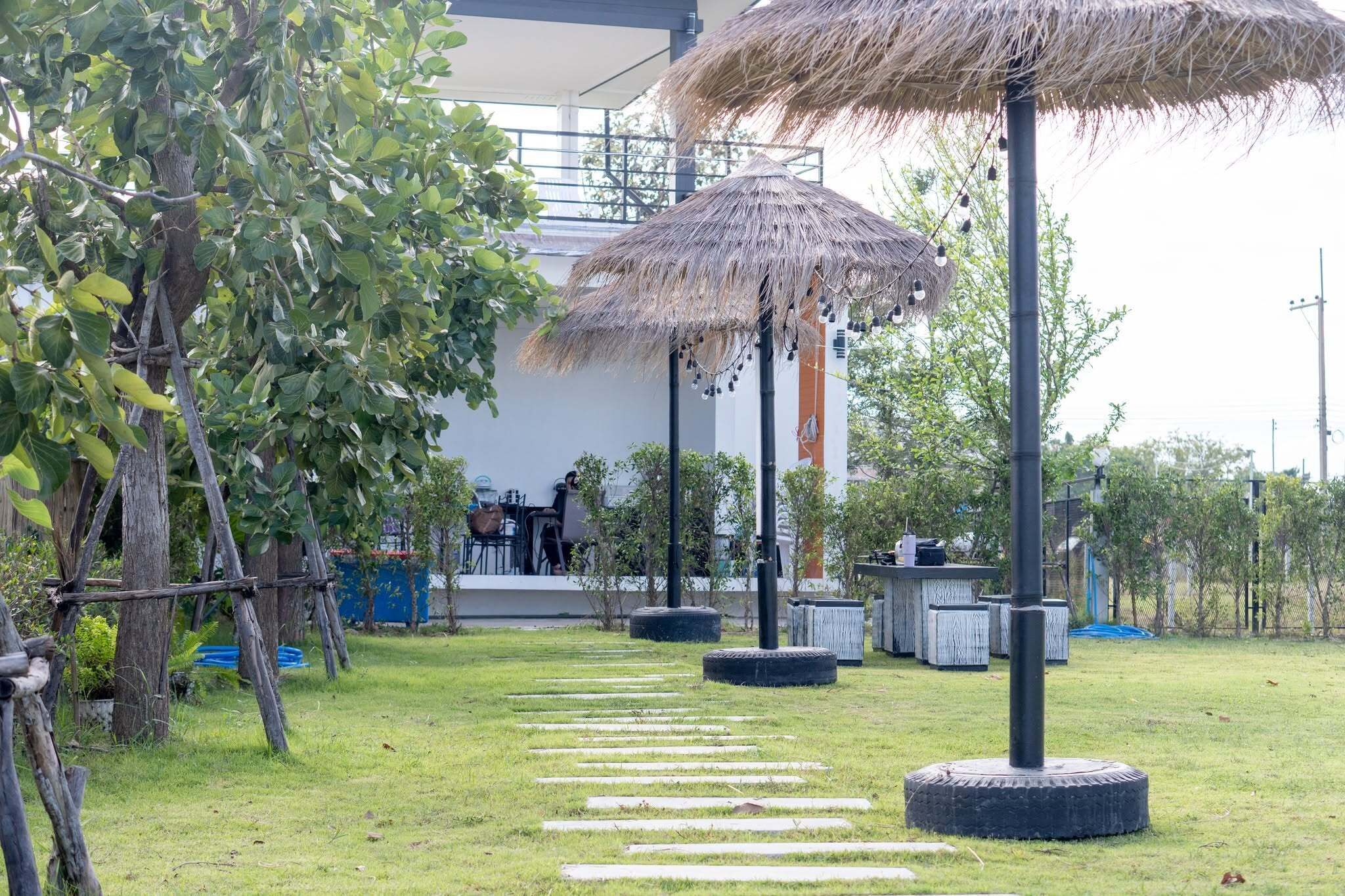 A grassy outdoor area with a pathway, trees, and a building with outdoor seating.
