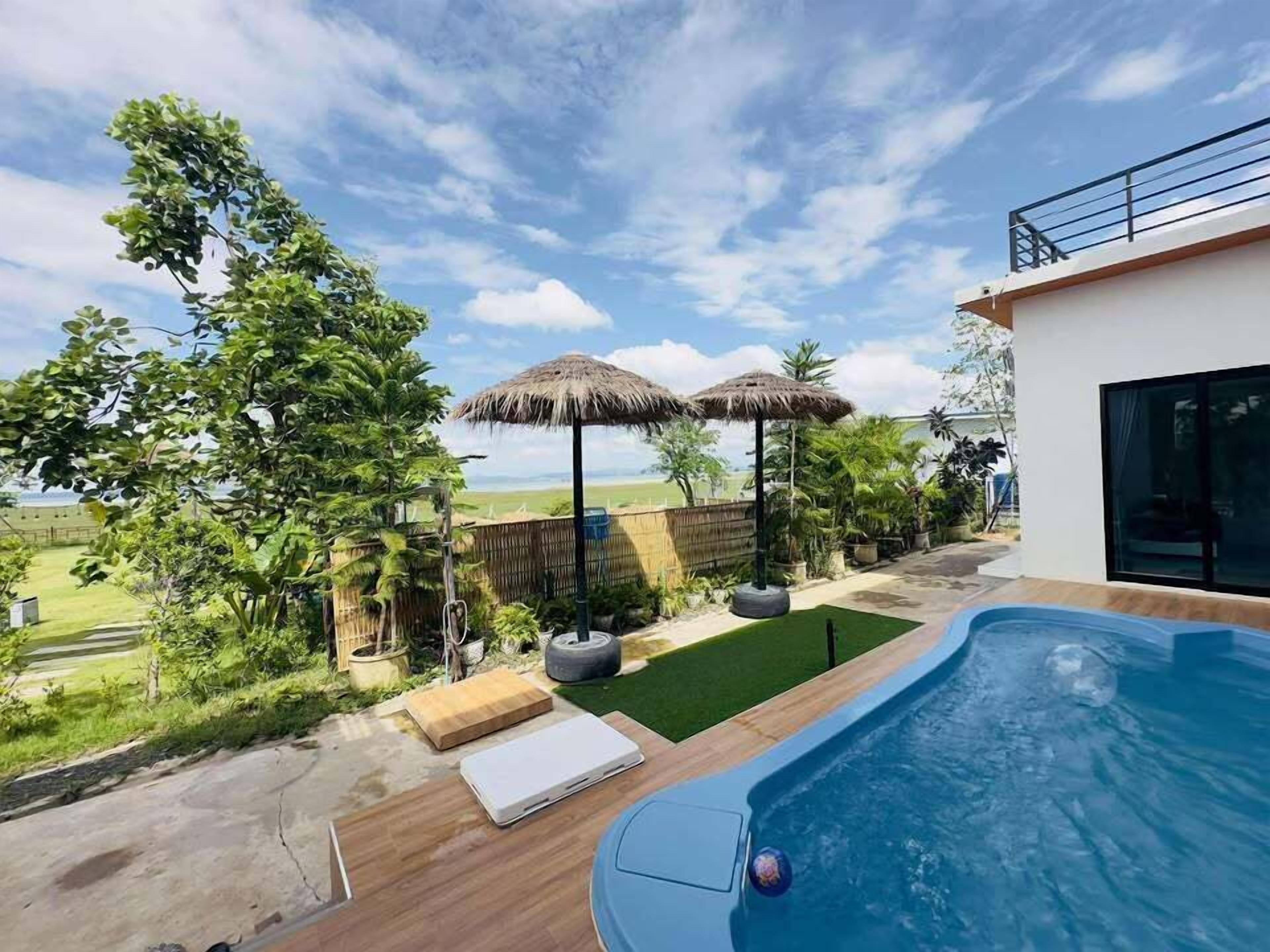 A swimming pool with a wooden deck, two thatched umbrellas, and a view of the landscape.