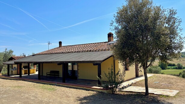 Un bâtiment d’un seul étage, doté d’un toit en tuiles, d’un patio couvert et d’un petit arbre en premier plan.