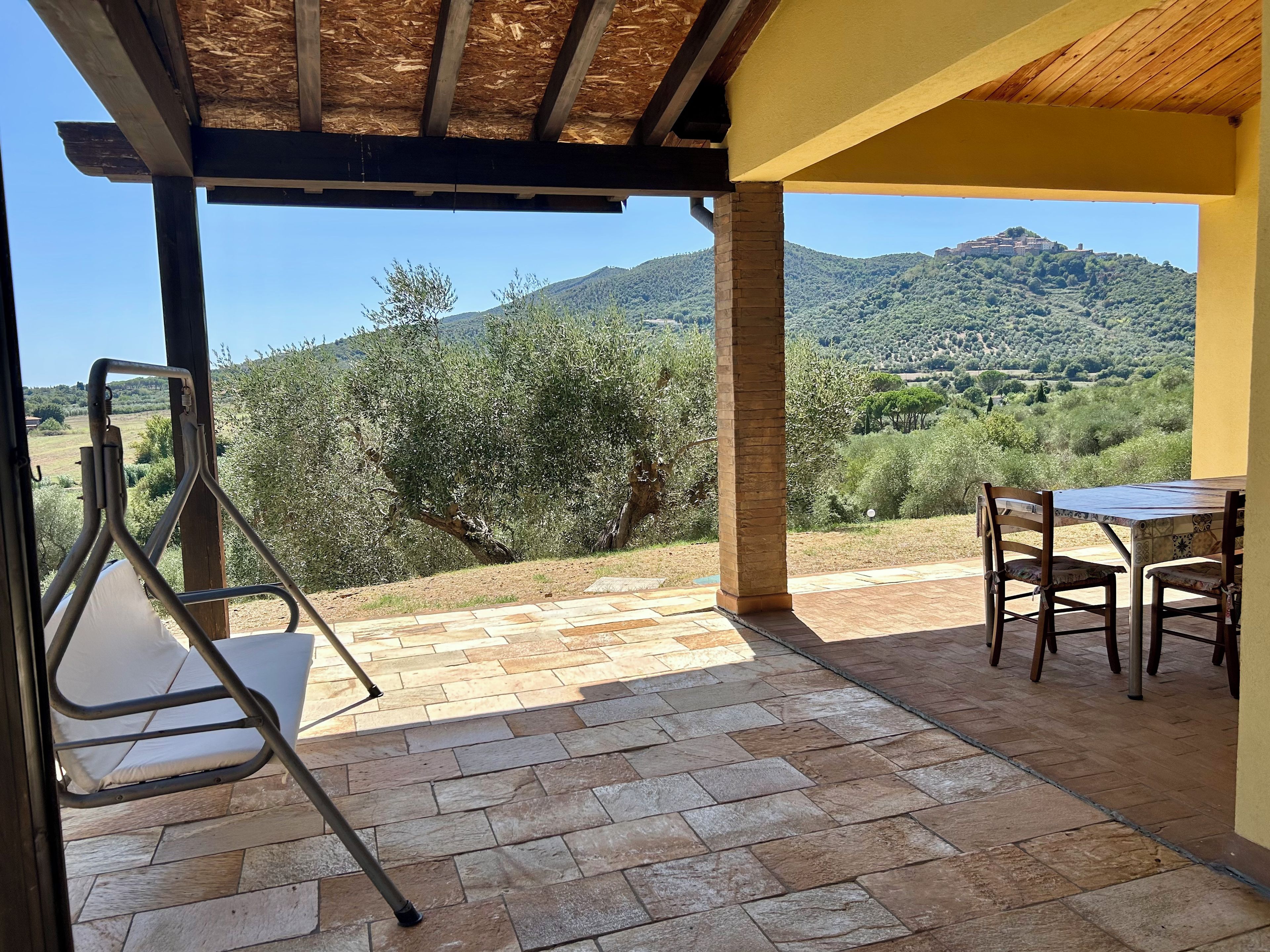 A covered outdoor seating area with a table and chairs, overlooking a mountainous landscape.